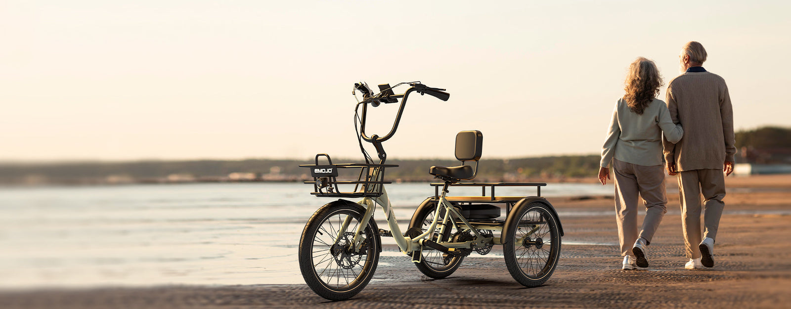 A couple walking beside an EMOJO trike on a beach at golden hour